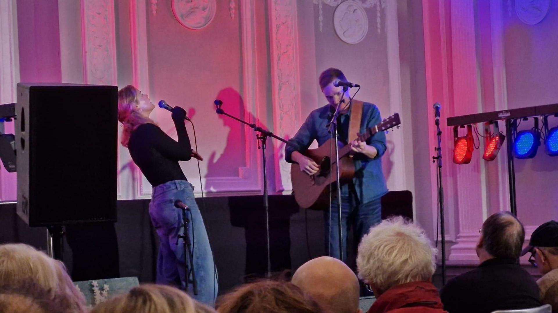 Two musicians performing on a stage with a crowd in front of them