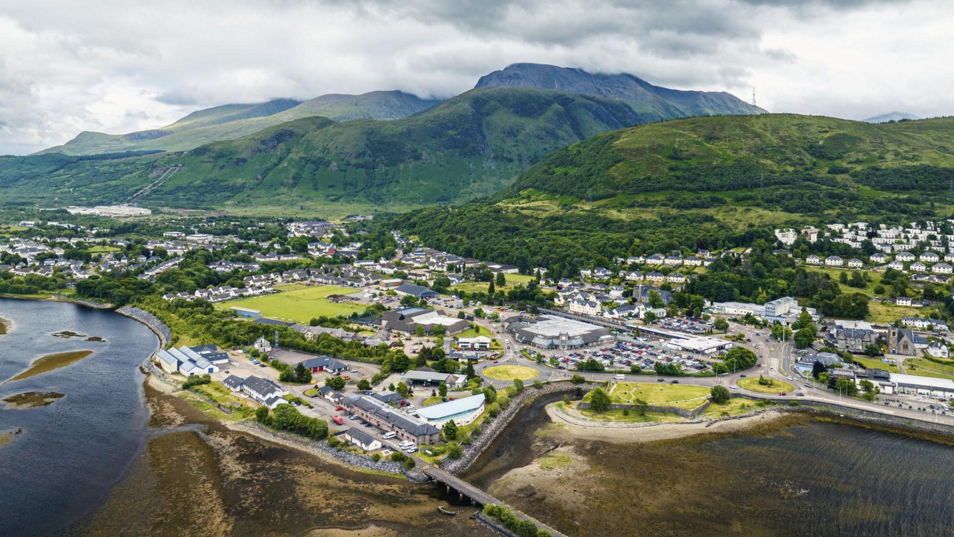 An aerial view of Fort William on the shores of Loch Linnhe with Ben Nevis and its neighbouring mountains in the background.