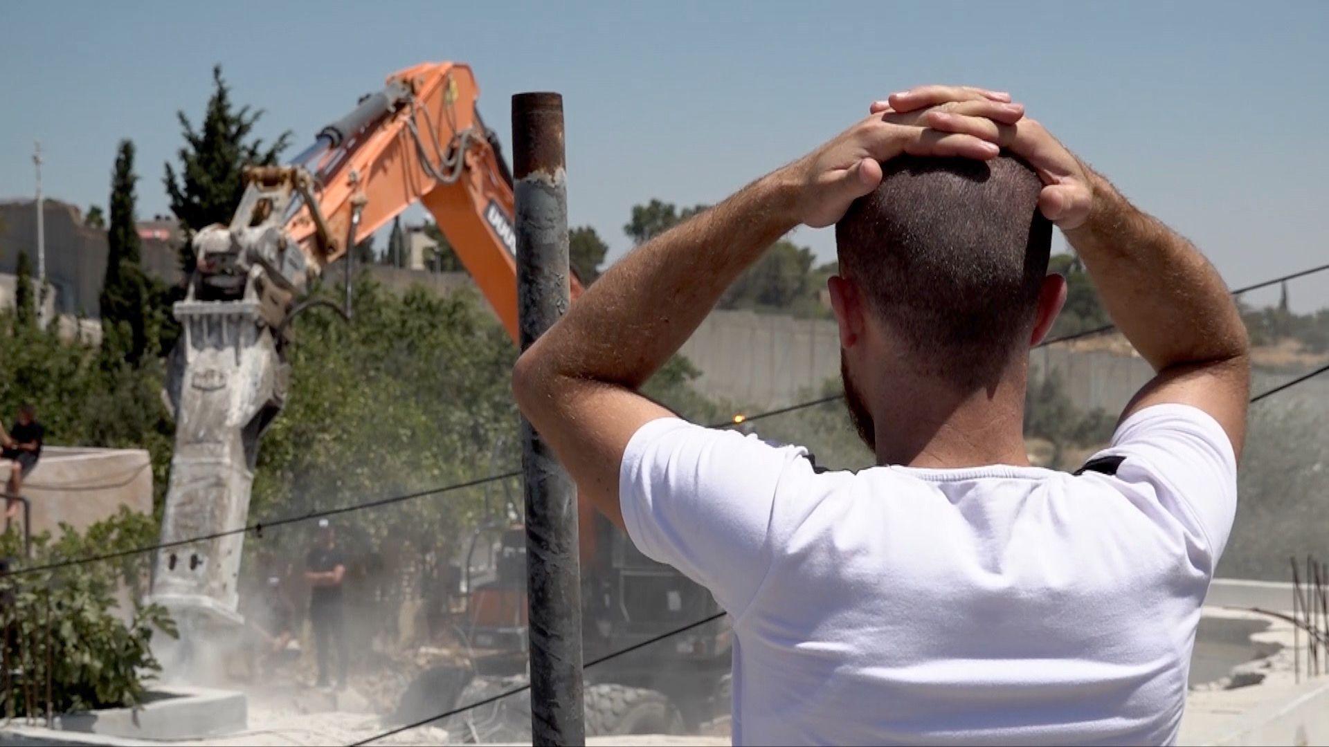 Ahmad stands with hands on head watching bulldozer demolishing his house