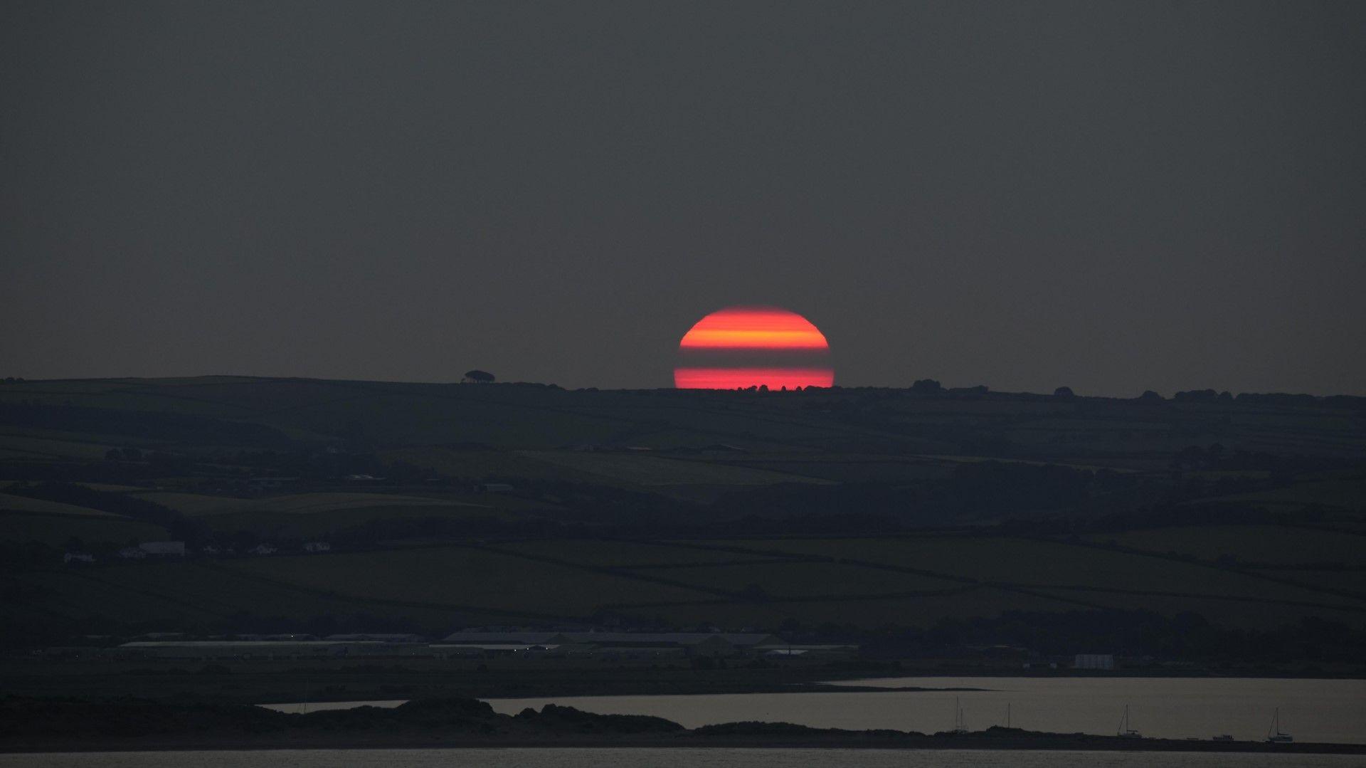 A red sun rises over hills