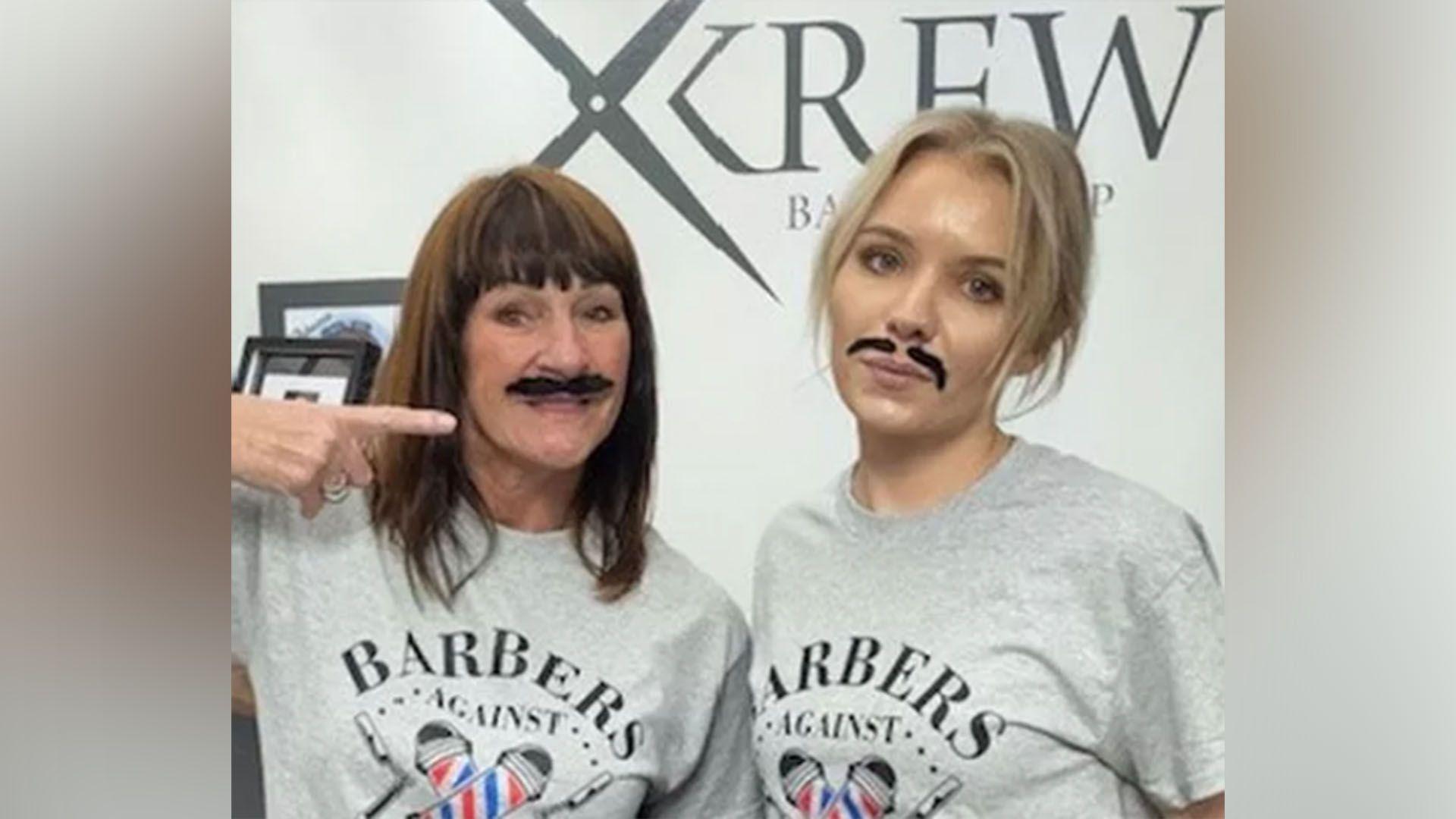 Two men wearing fake moustaches look down the camera.