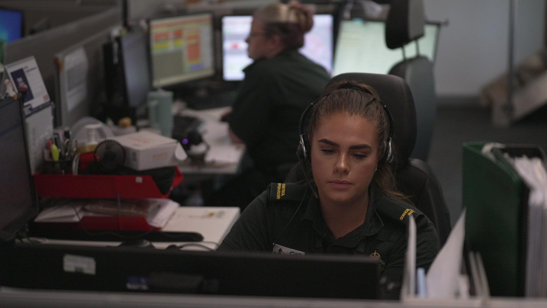 Emergency 999 call handlers in an office sitting at computers with headsets on their heads.