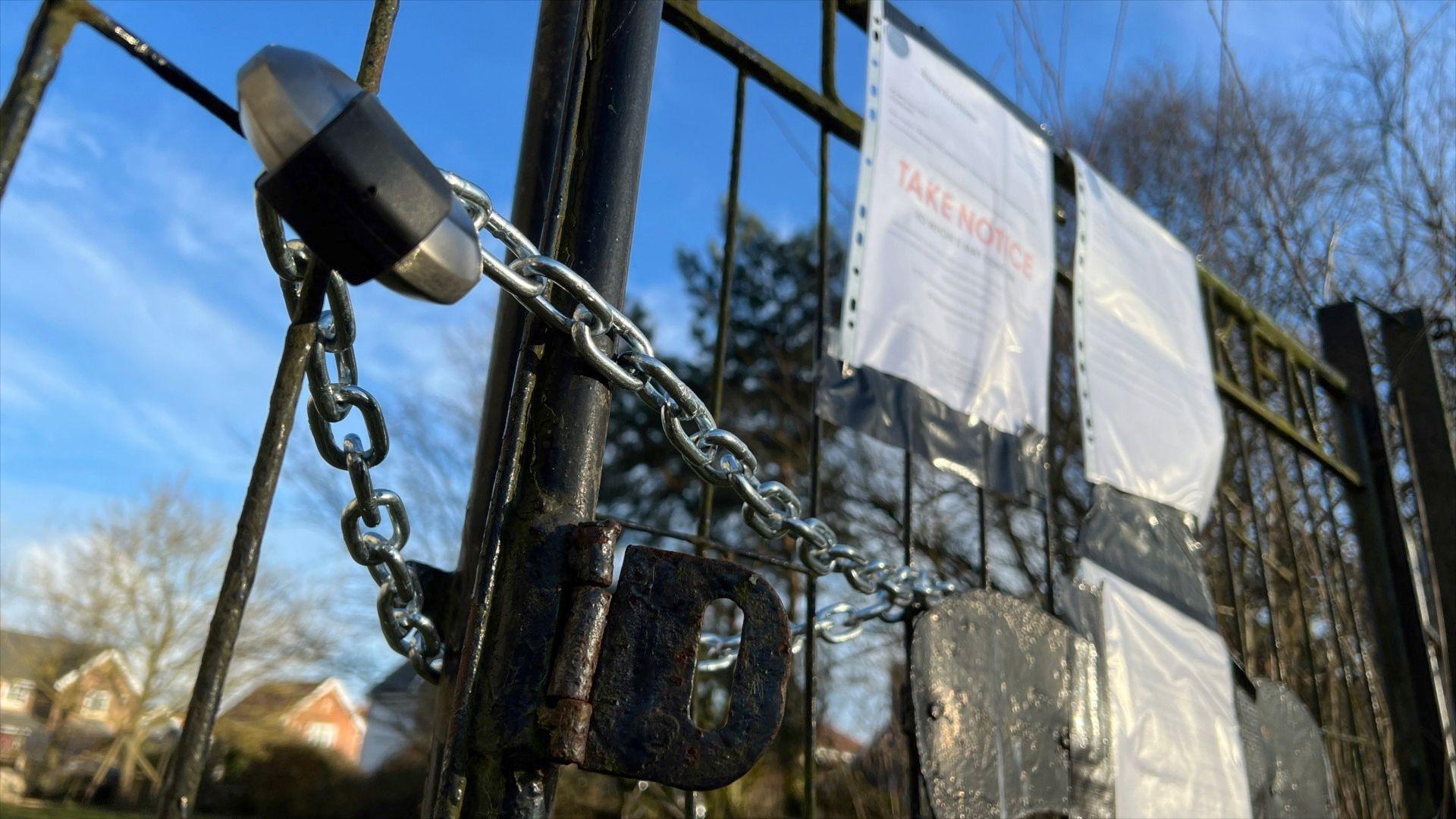 A metal gate with a padlock through the bars. On the gate are three pieces of A4 paper which are eviction notices