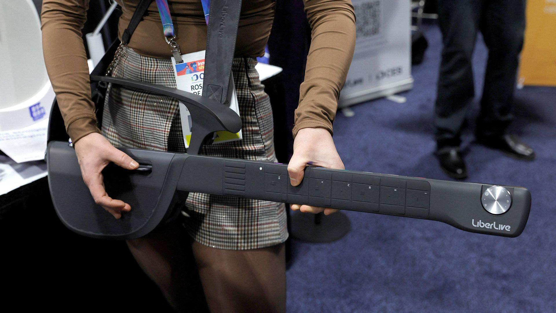 A person playing an electronic instrument in the shape of a guitar but without strings