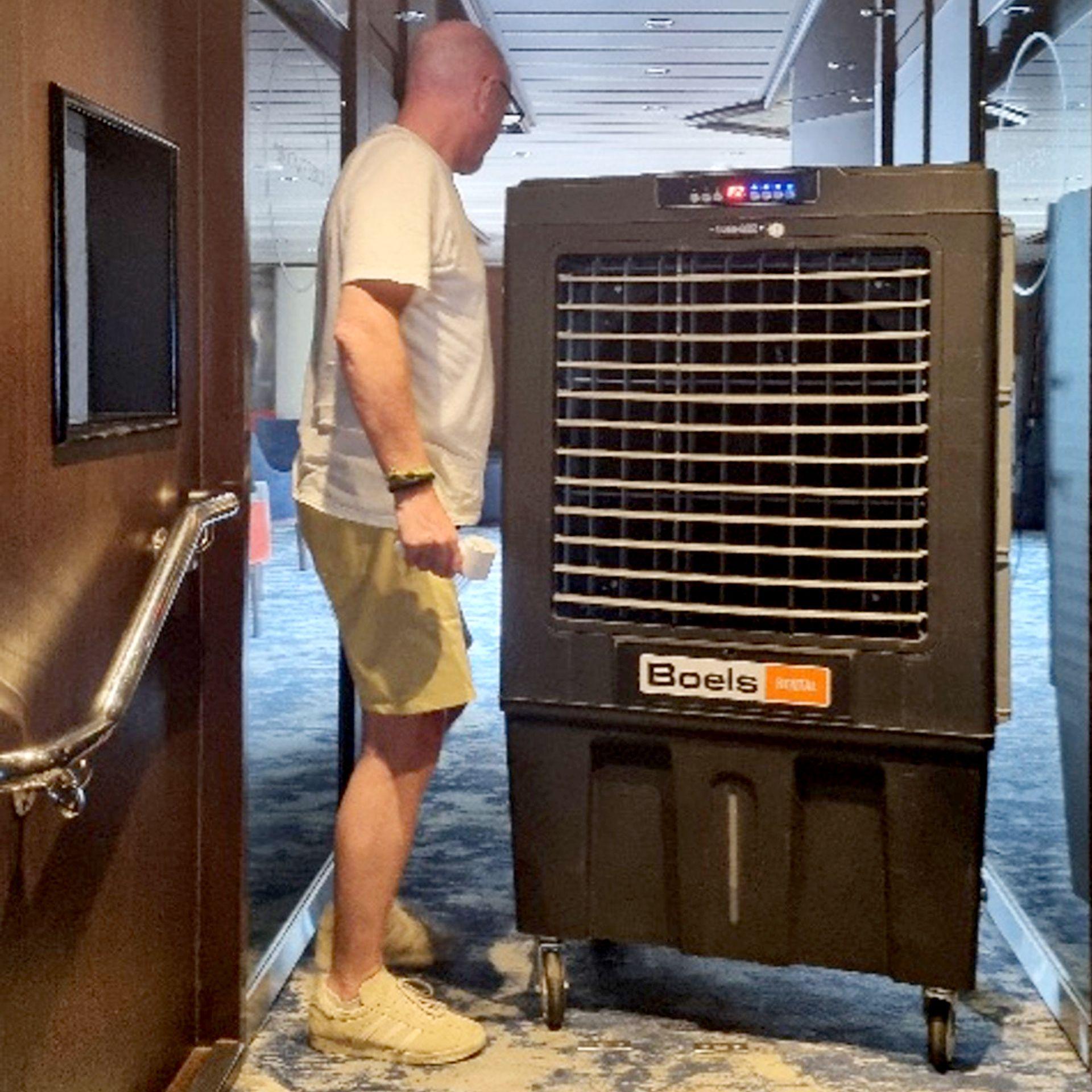 Man walks around a large air conditioning unit in a corridor onboard a cruise ship