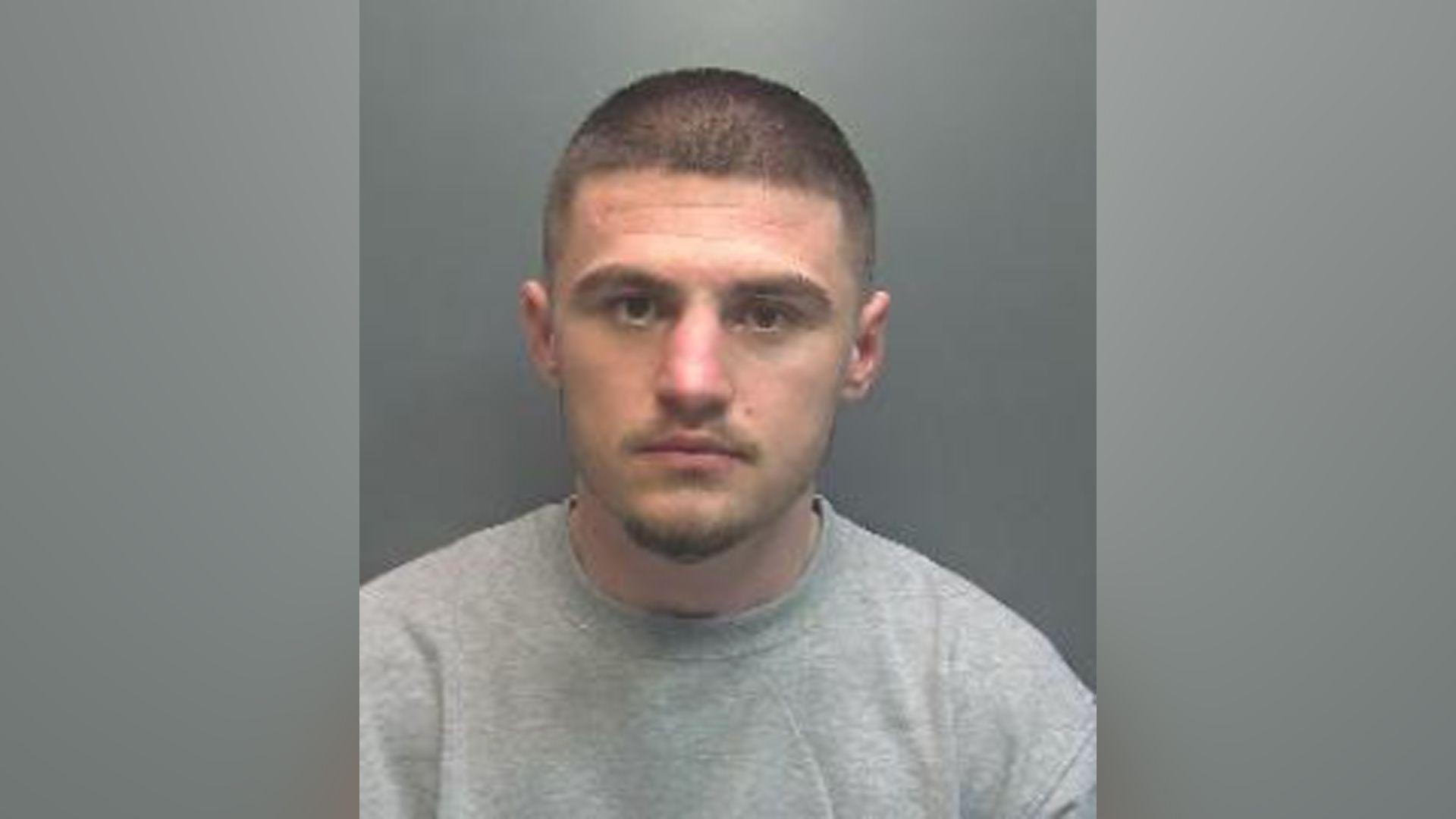 A police mugshot of a man with short hair and a light beard.