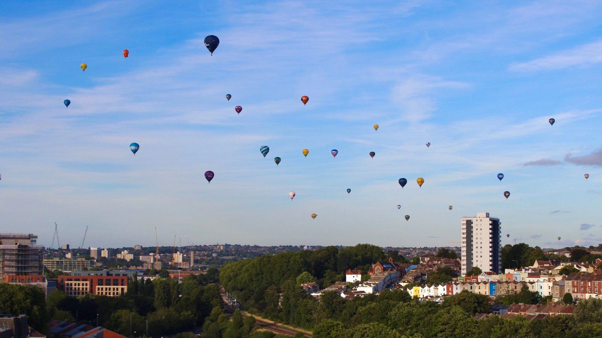 Tens of hot air balloons float above Bristol on a summer's day, taken from a rooftop in Bedminster