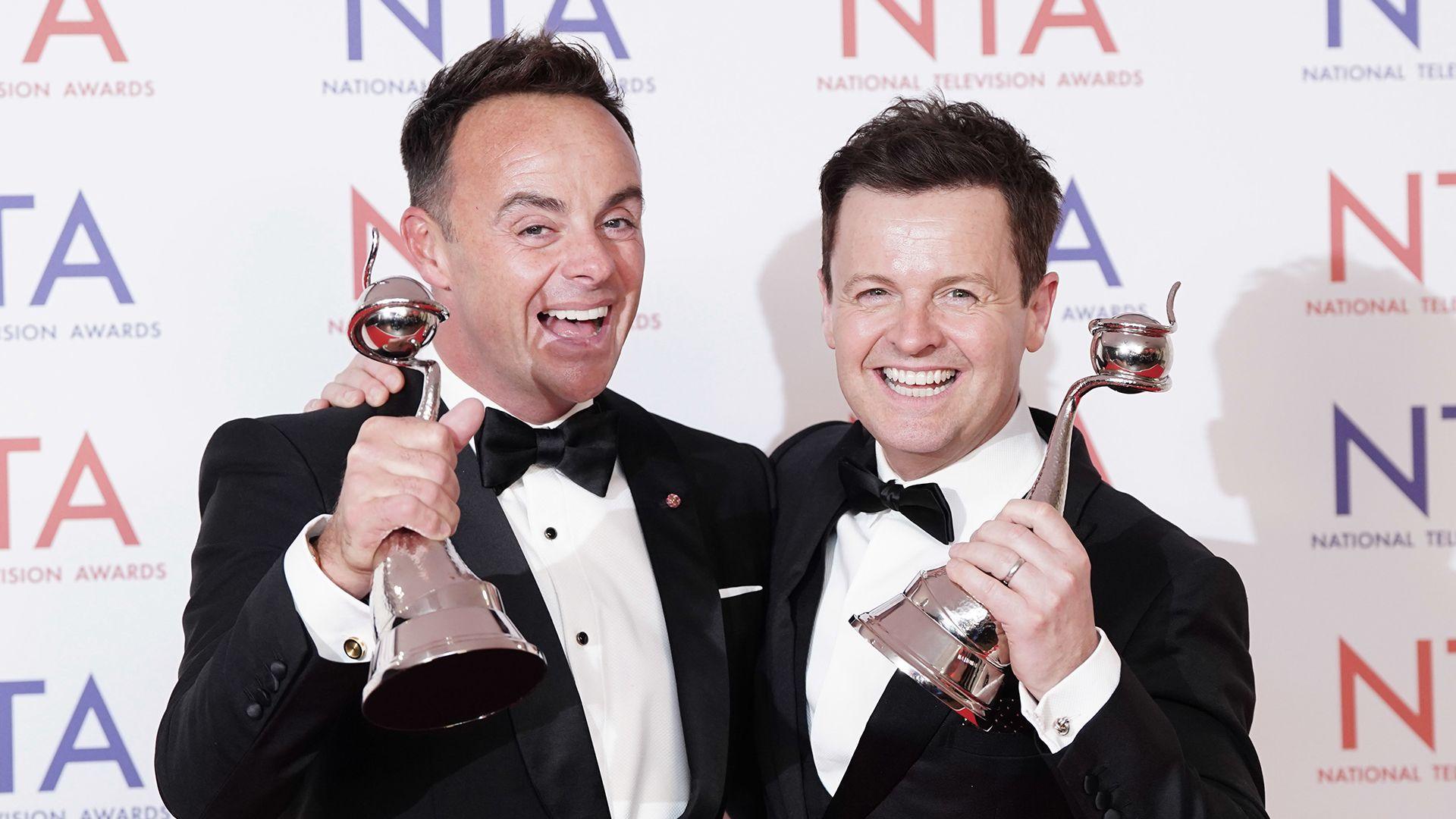 TV presenters Ant and Dec in suits, holding their awards trophies, smiling