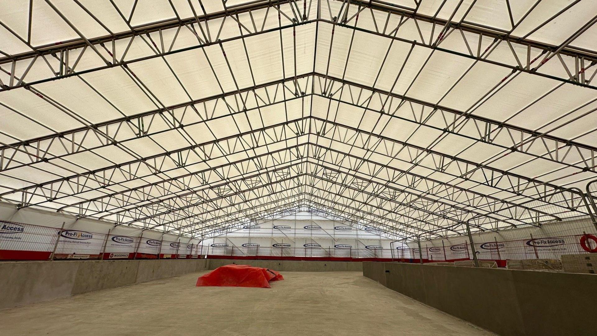 Large concrete walled pool area with red sheet towards on end - it is covered in a scaffold structure and white plastic sheeting