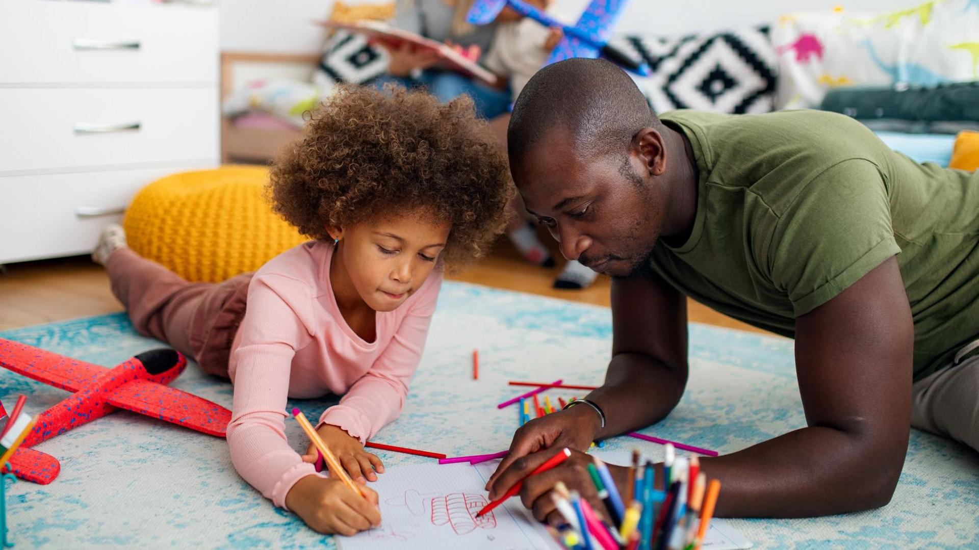a child and parent colour paper together on the floor
