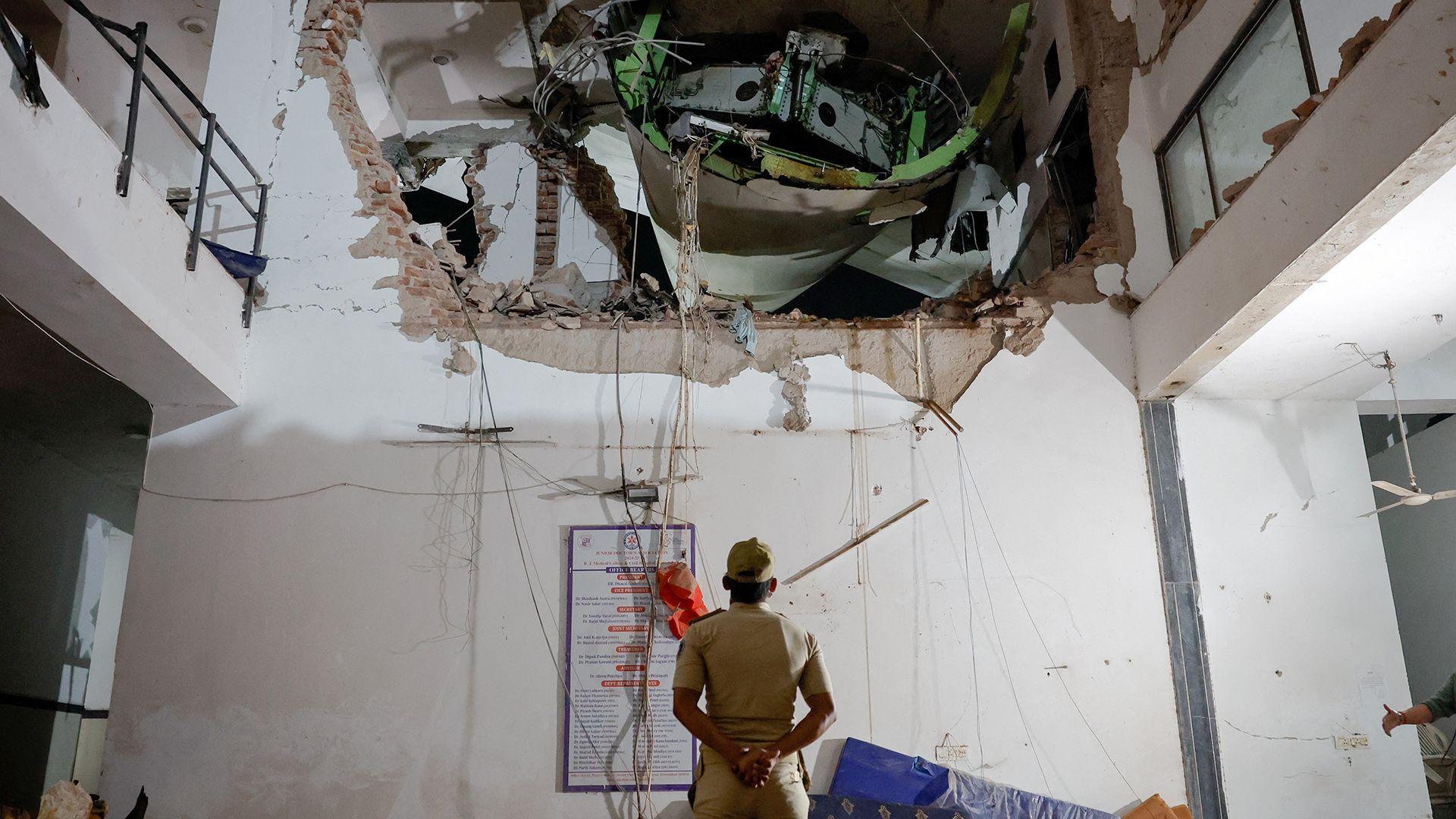 An official looks up with his arms behind his back and back turned to the camera, as they inspect a huge hole in the wall of a building interior, with some of the plane visible in the hole, on Thursday.