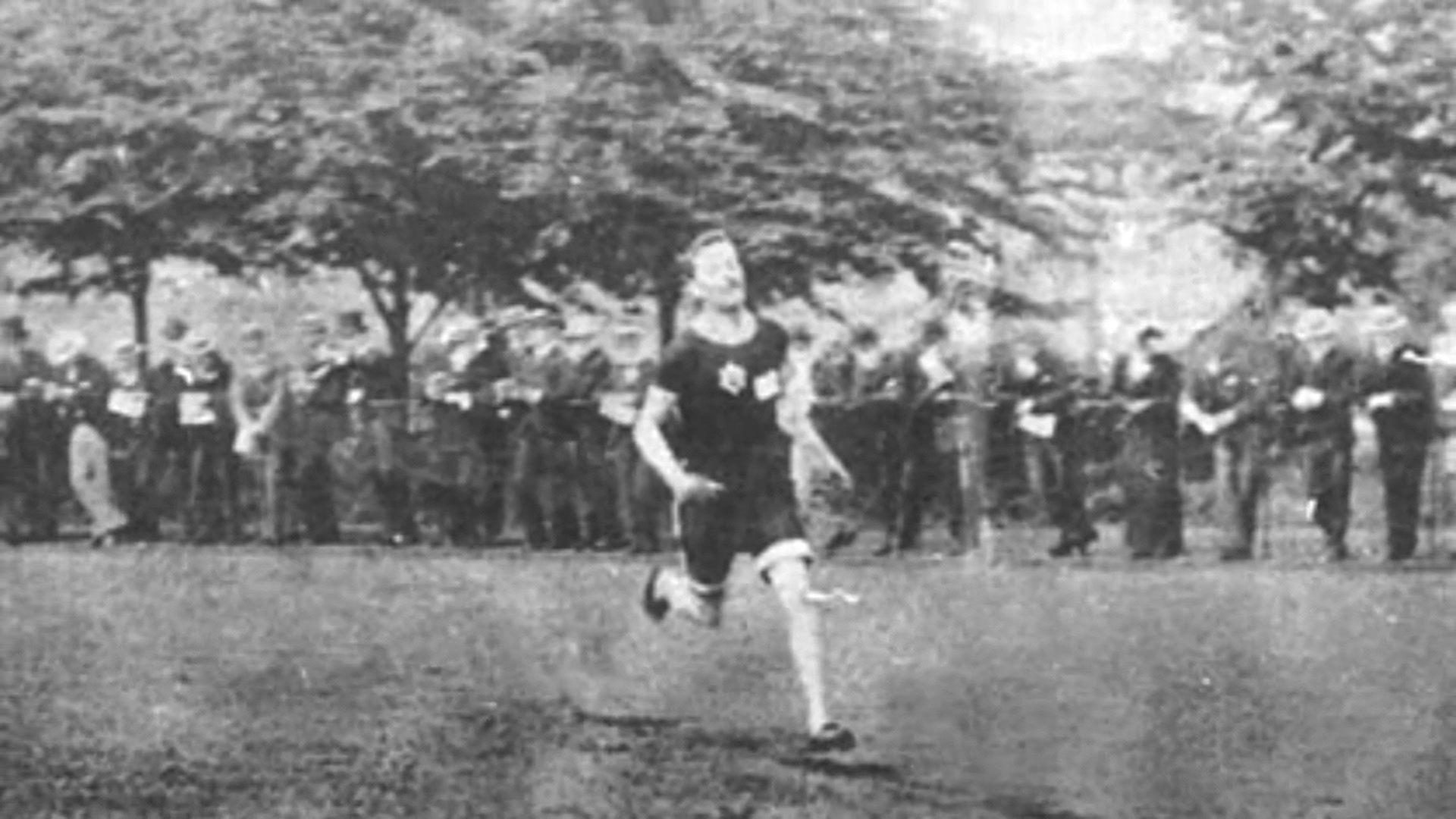 Fuzzy black and white photo of Charles Bennett running in front of a crowd of people standing on the side lines