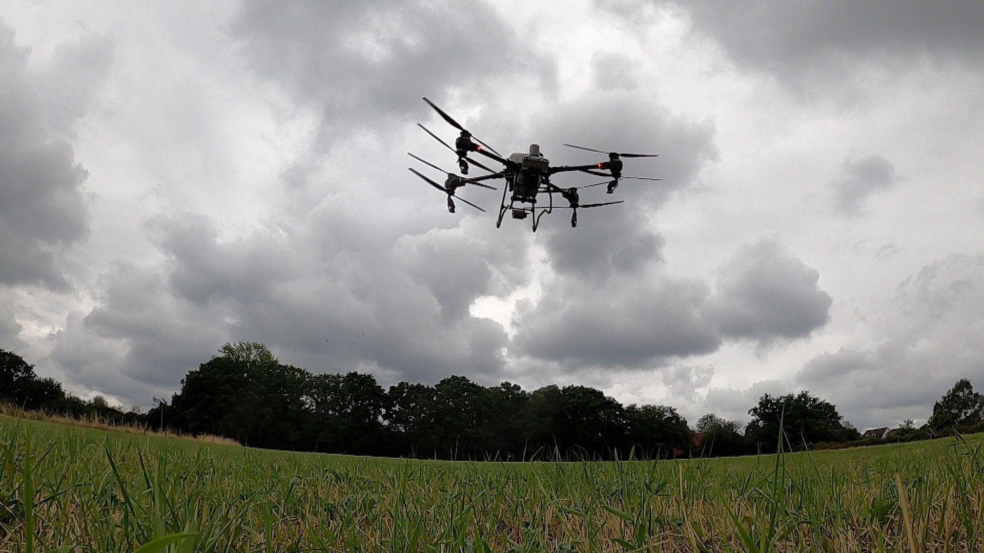 A farming drone flies over a field spraying liquid from four nozzels as it follows a planned route