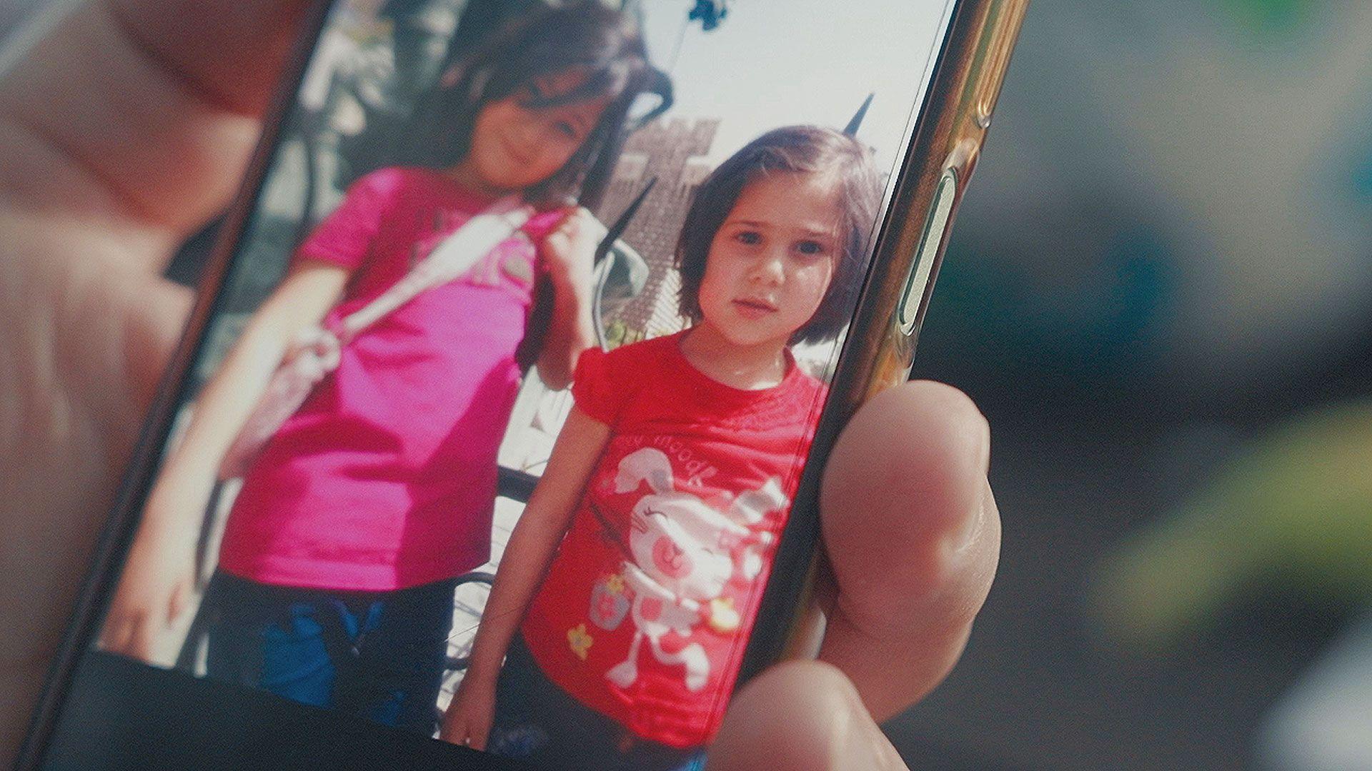 Two little girls with dark hair and in pink and red t-shirts smile for the camera in a photo shown on a mobile phone.