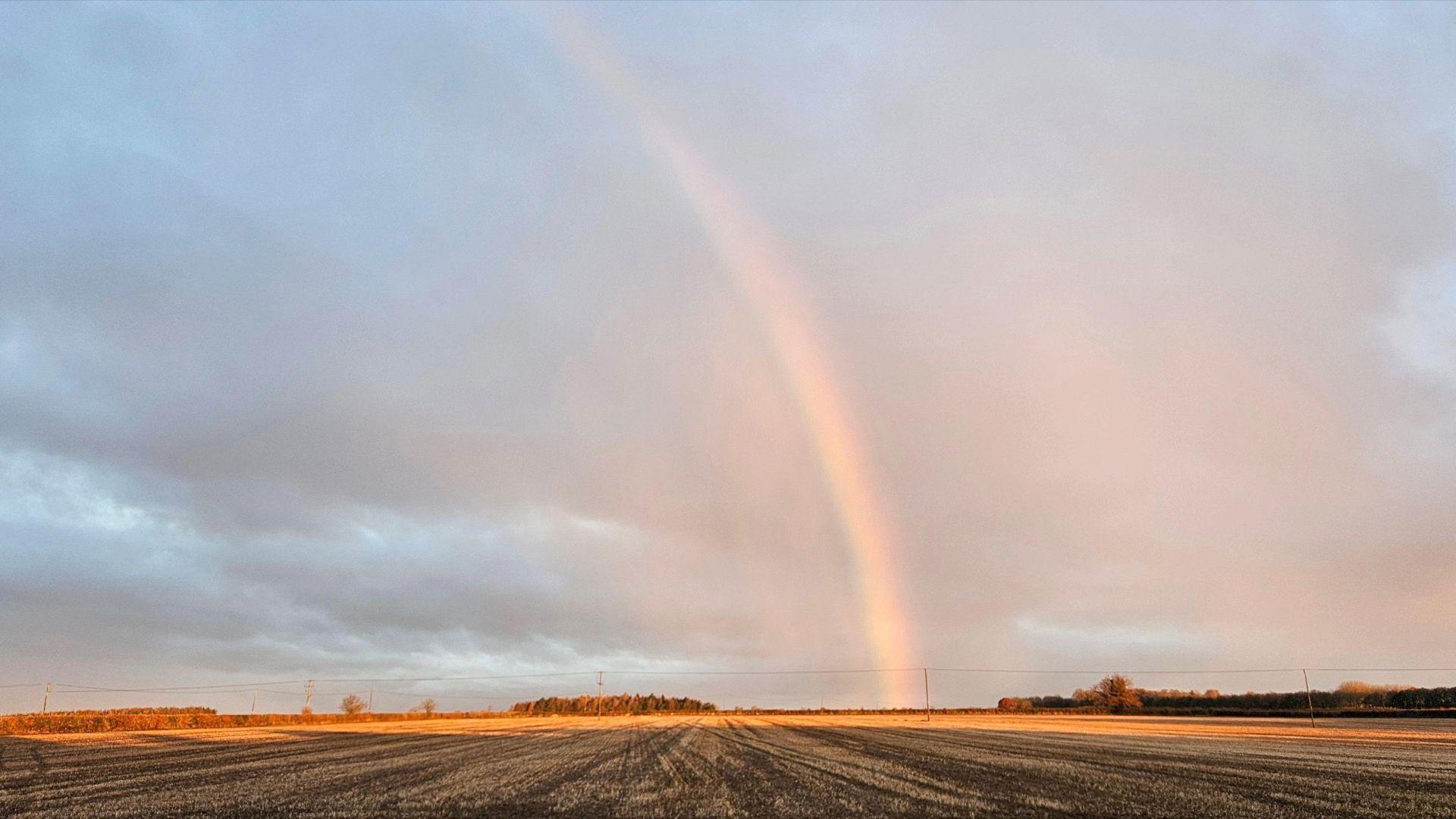 A Rainbow is seen over fields landing in fields with orange glow of the sun at Painswick in Gloucestershire