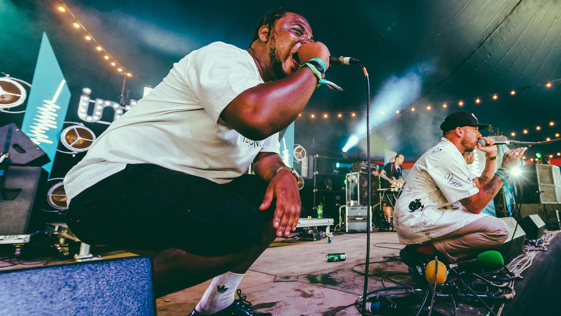 A man on stage crouching and shouting into a microphone