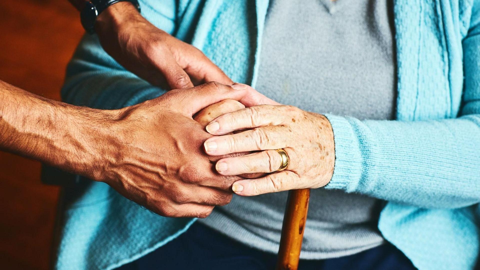 A care worker holds the hands of an elderly person in theirs