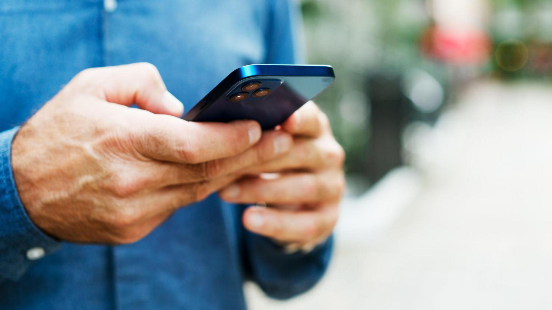 Close-up of a man wearing a blue shirt holding a blue mobile phone