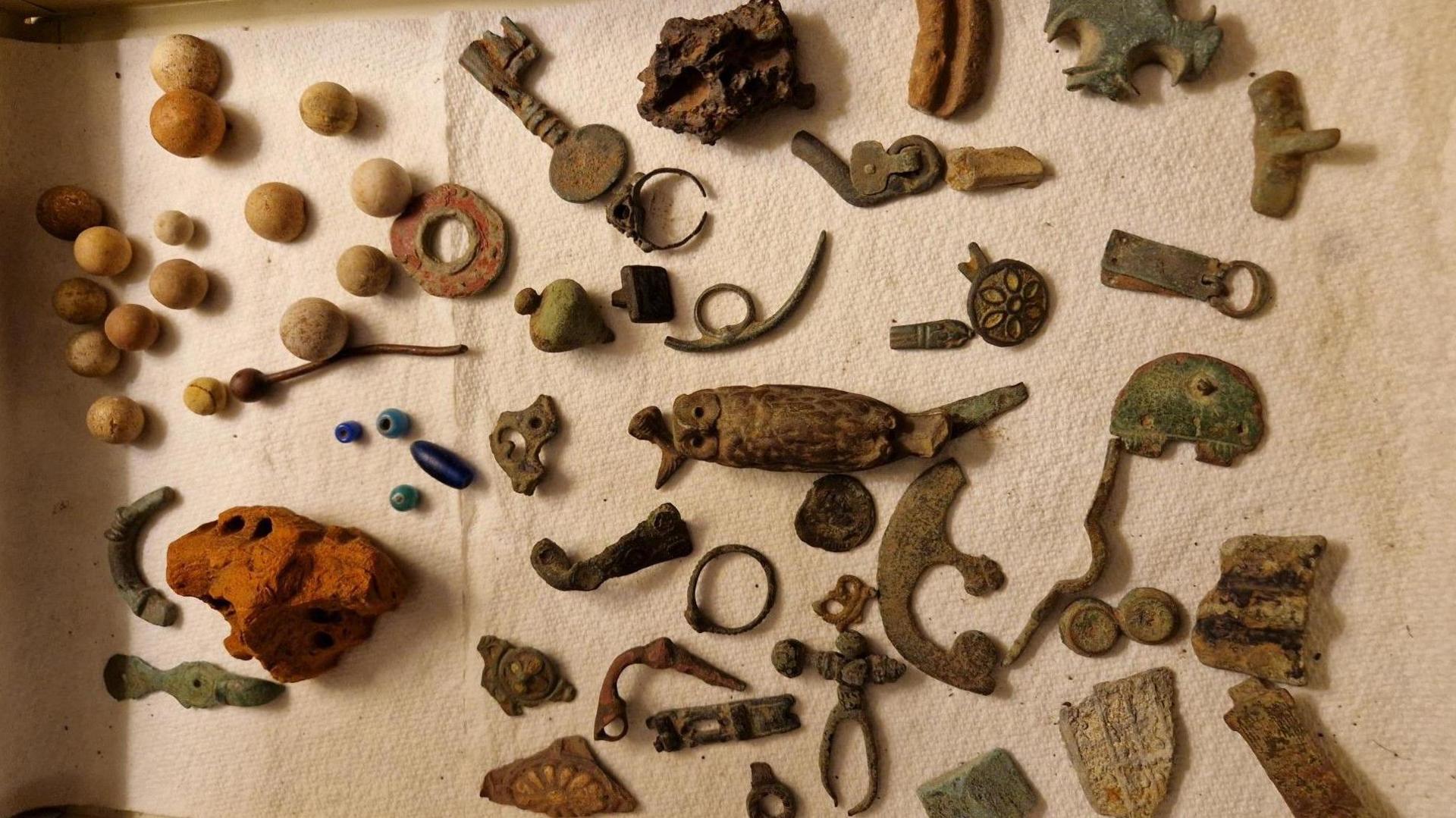 A tray, lined with white textile, on which are carefully laid out a number of small metal and pottery items