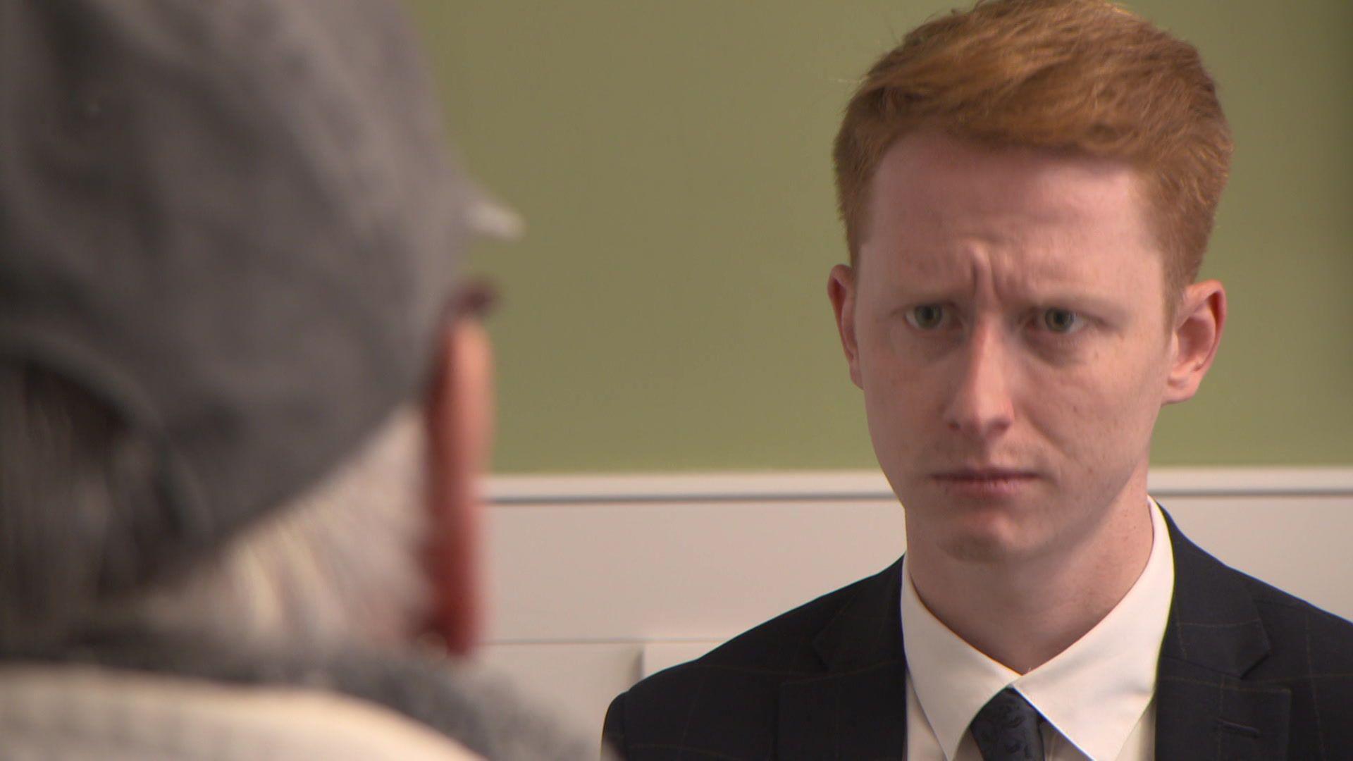 "Jane" being interviewed by the BBC's Andy Watson. Only half the back of Jane's head is visible, to protect her anonymity. She is wearing a grey cap and thick clothing. Watson has neat, short red hair and is wearing a black suit, white shirt and black tie.