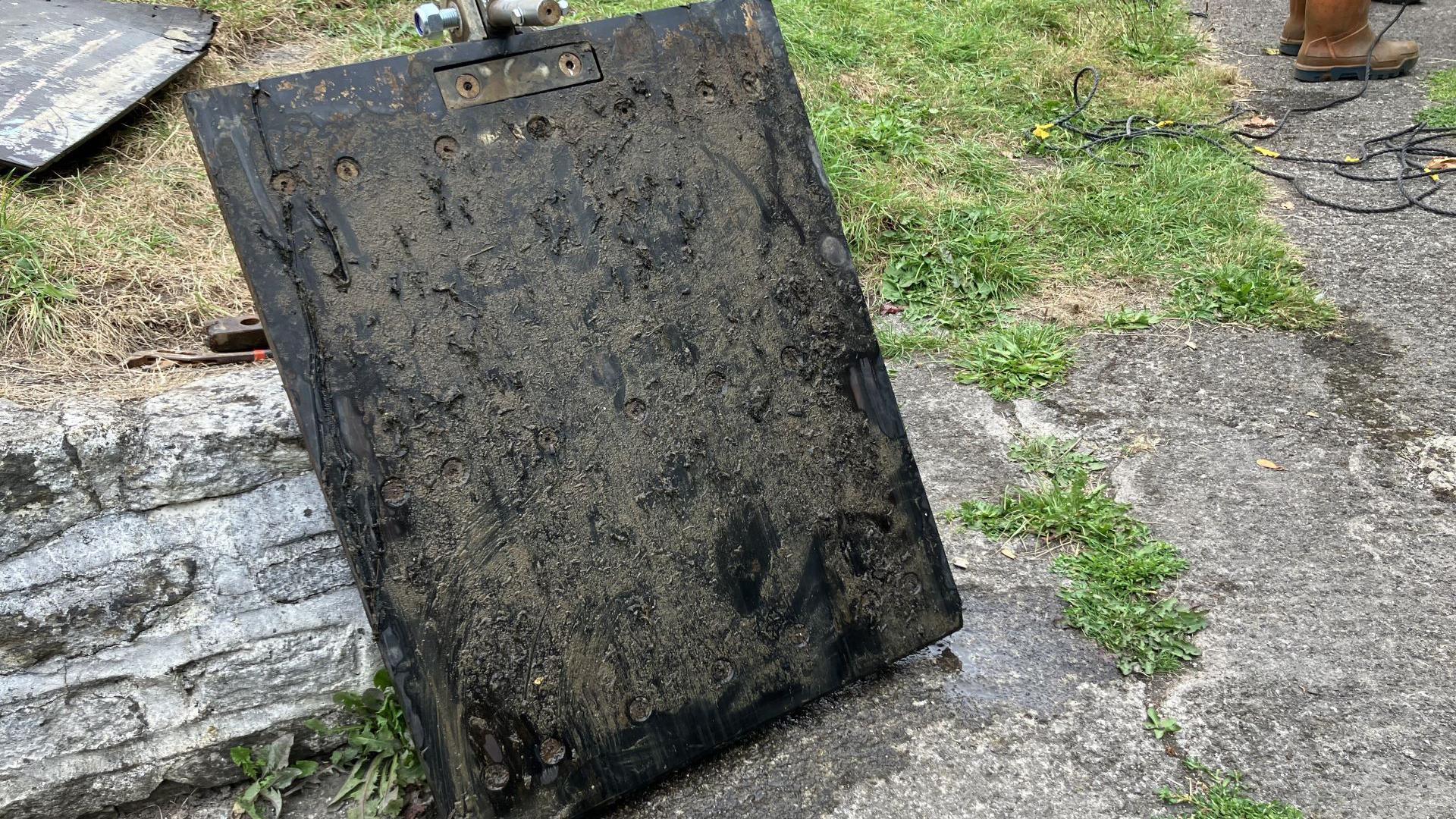 Black rectangular panel leant up against a low stone wall