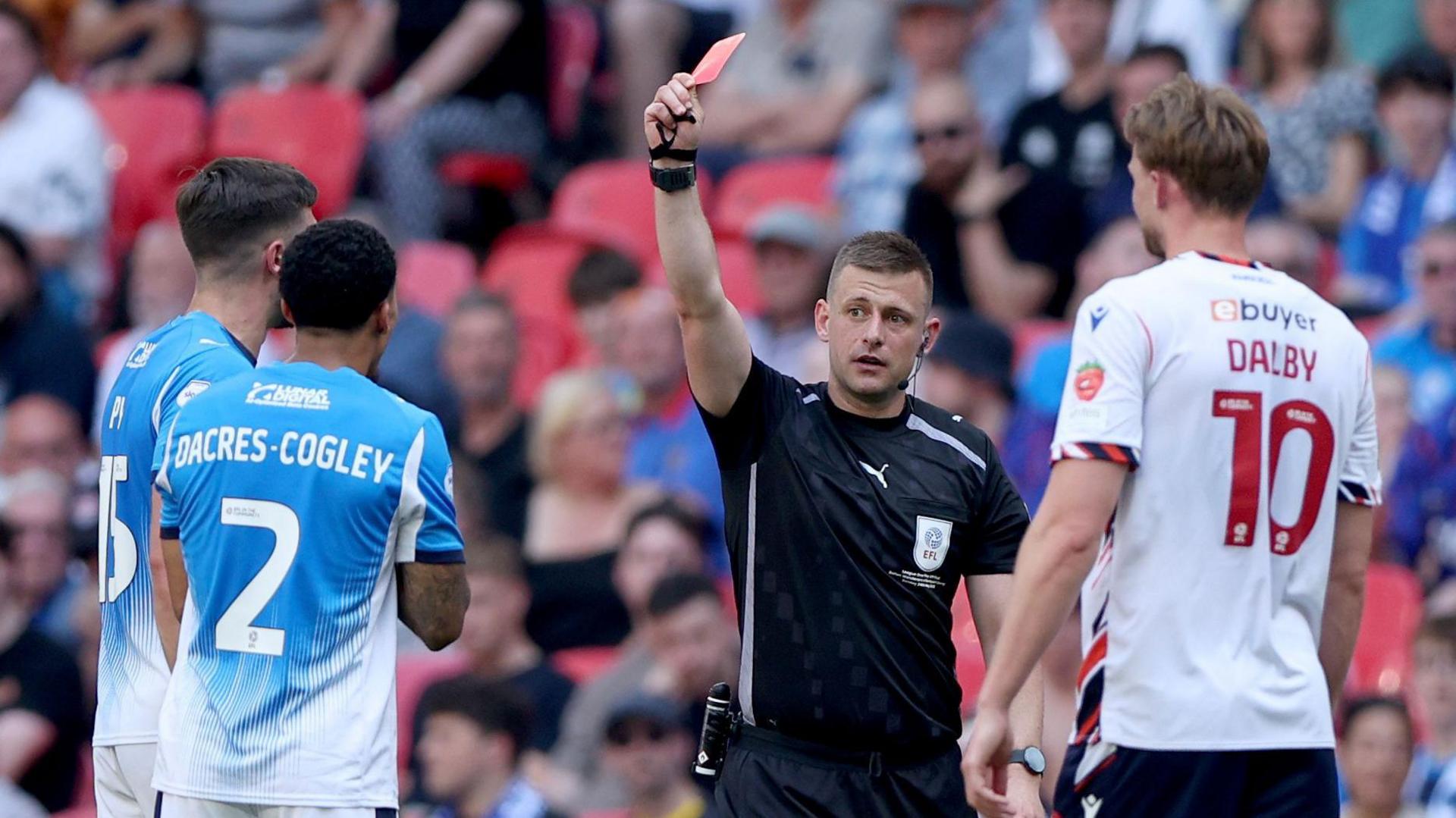 The referee holds up a red card to Josh Dacres-Cogley after a hair pull on Ibrahim Cissoko at the League Two play-off final at Wembley