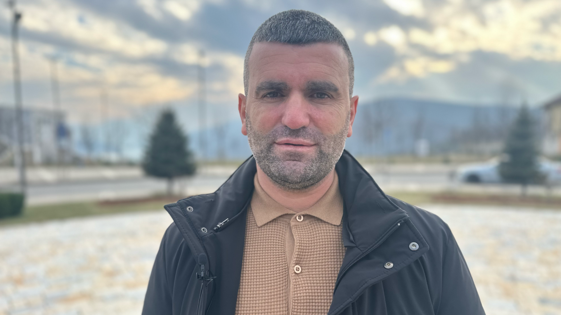 Albert Halilaj, the Mayor of Kukës, is standing outside a large roundabout in the middle of the town with mountains in the background 