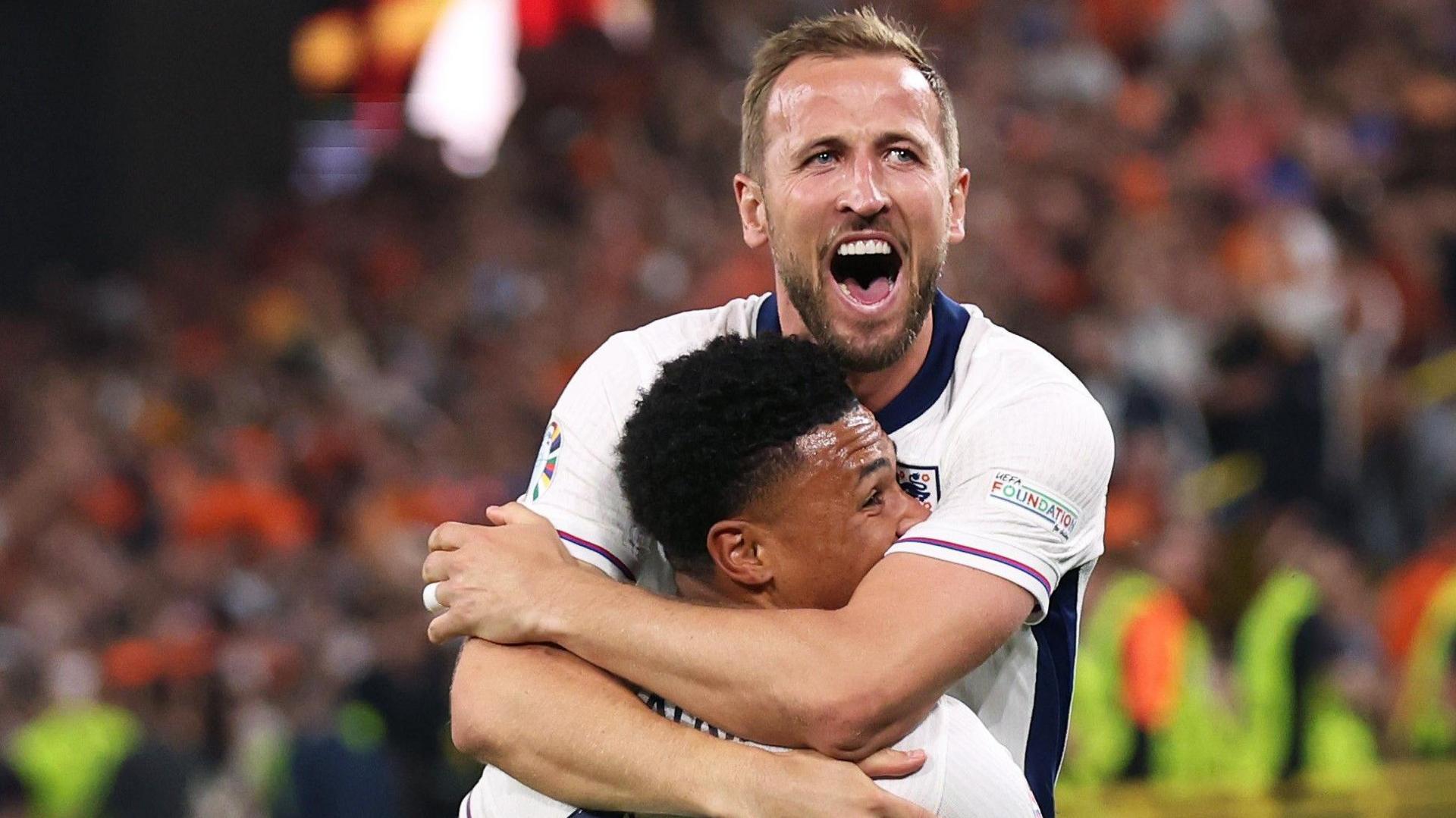 Harry Kane and Ollie Watkins celebrate an England goal with Kane jumping around Watkins with his arms around his neck. 