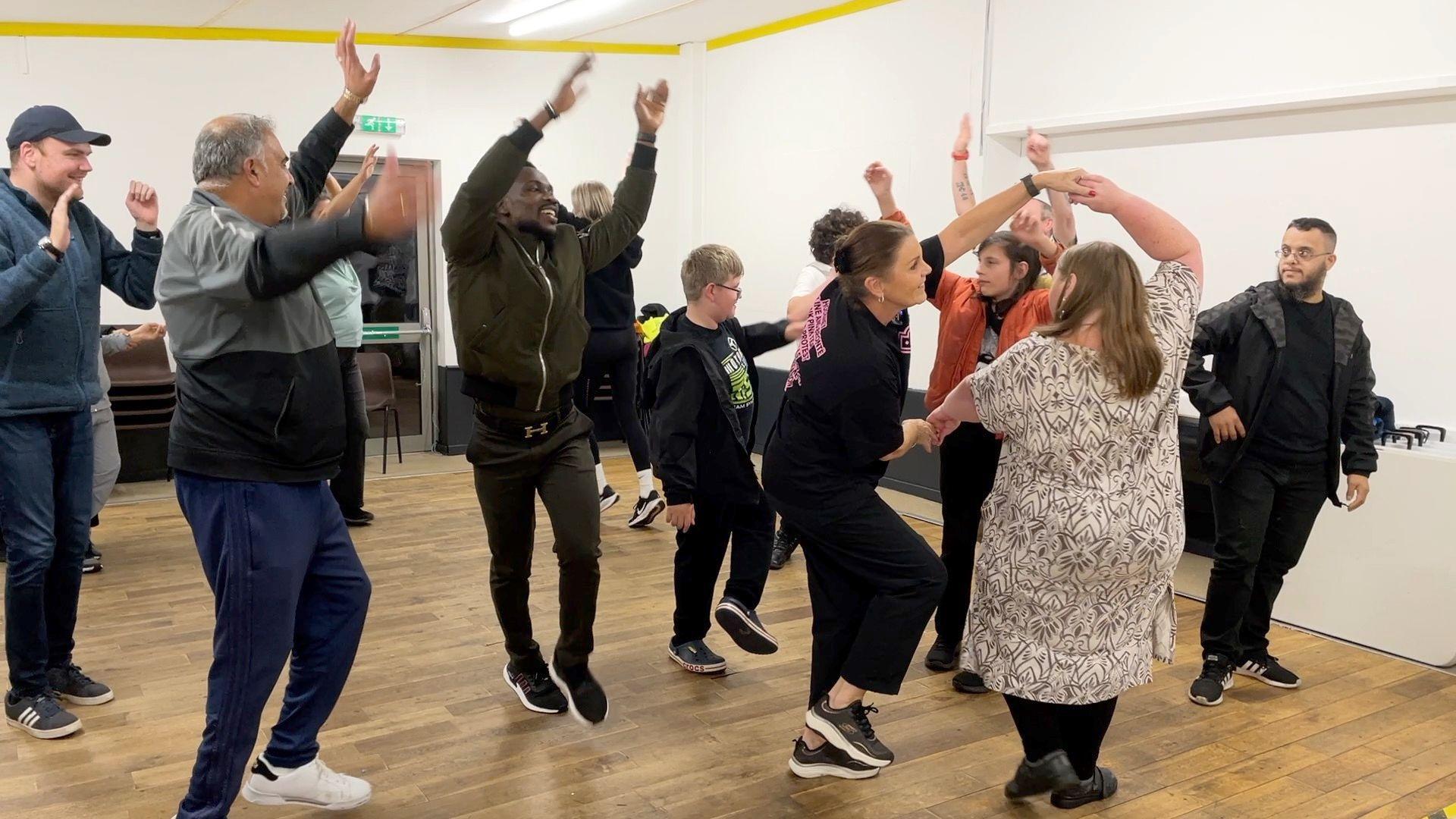 Members of Bradford Phab Club learn African dance. They are all of different ages, genders and ethnicities.