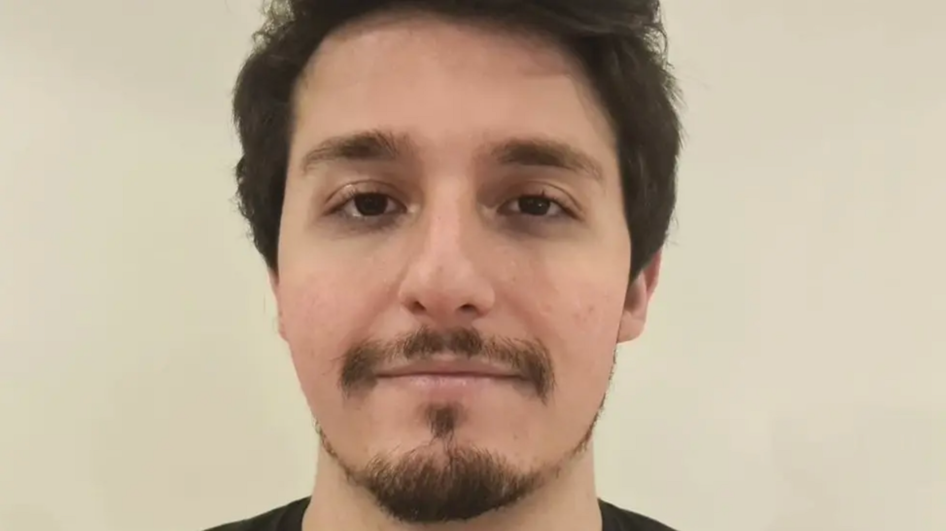 Head shot of Jonathan Reuben in front of a white/beige wall. He has brown hair and eyes and is looking directly at the camera with a slight smile.