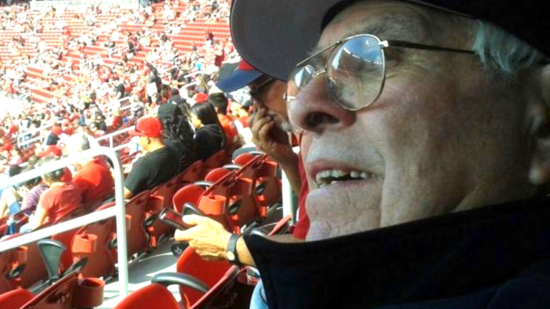 A picture of Raphael Cull in black hat and jacket and glasses, in the stands at a football match with crowd in background 