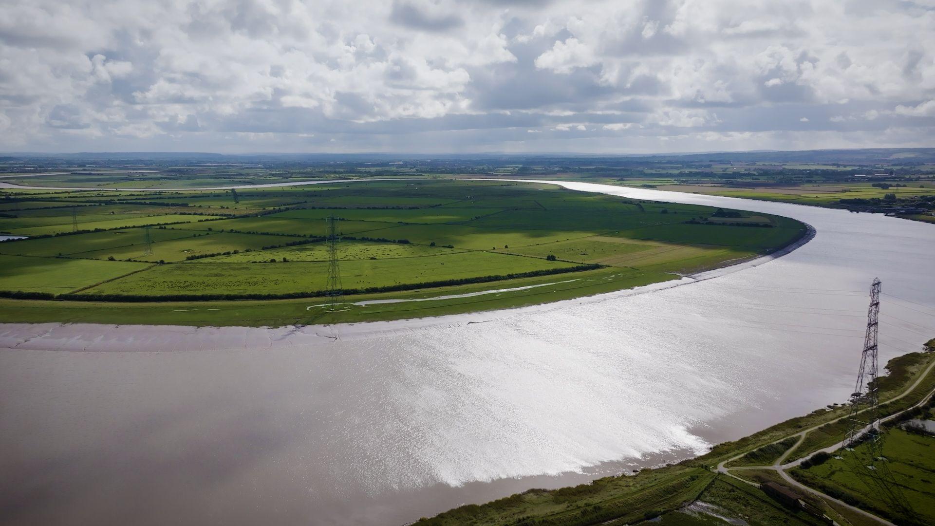 Overheads drone shot of the proposed site, with a swooping u-shaped river flowing through a vast green space