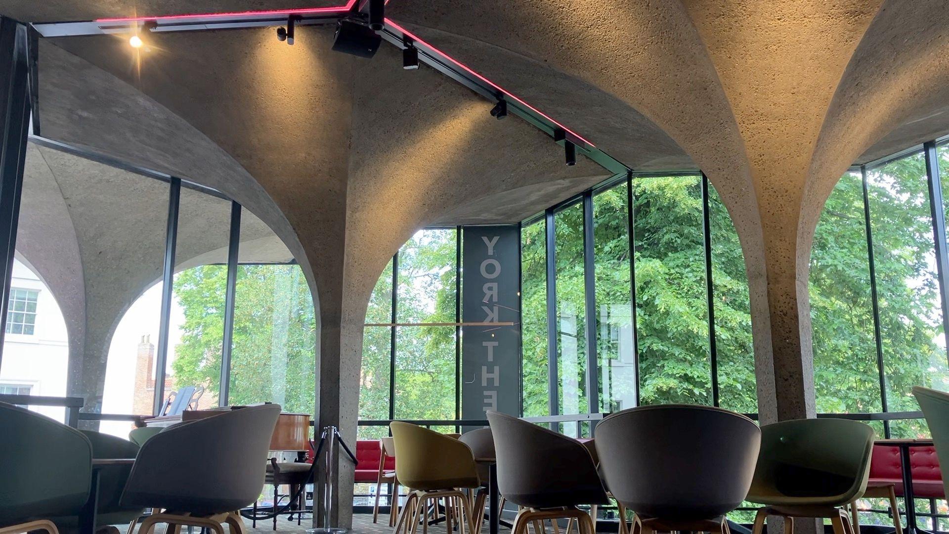 The cafe area of York Theatre Royal with concrete pillars replicating the medieval ones, along with chairs.