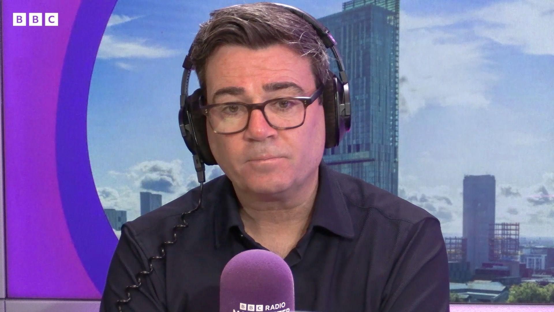 Andy Burnham, a man with dark hair in a black shirt, talks into a purple microphone on BBC Radio Manchester. 
