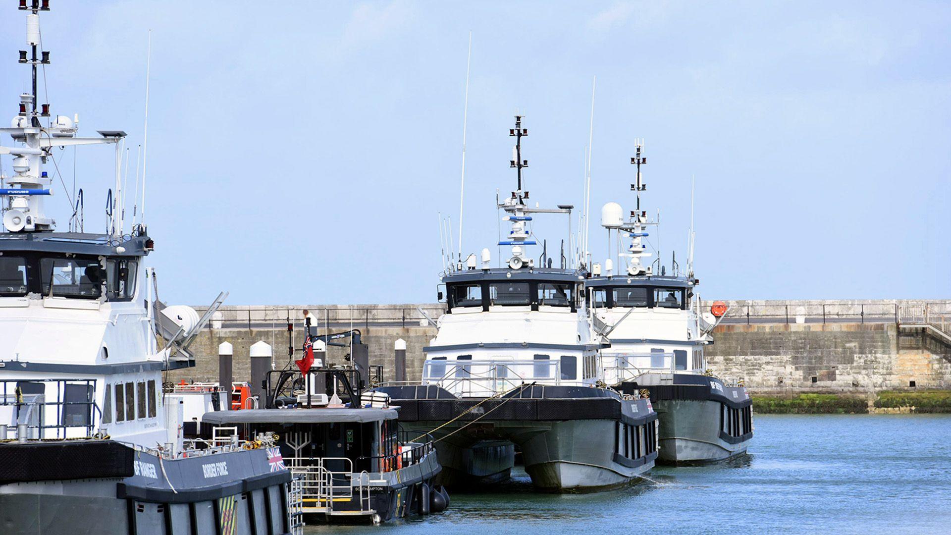 Three Border Force vessels are moored side by side in a harbour.