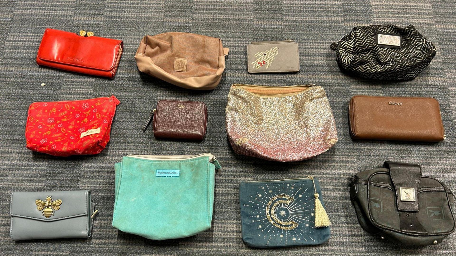 An image of 12 handbags, ranging in colour from red to brown, laid out on a grey carpeted floor