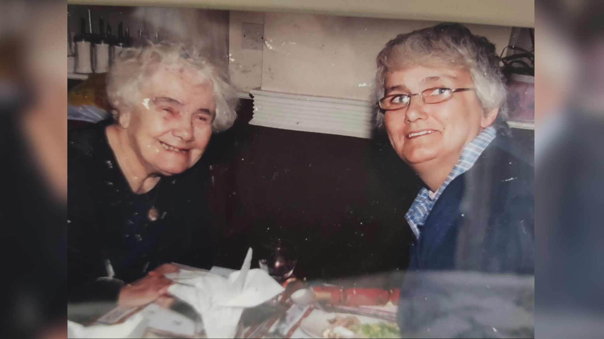A grainy old photo of Patricia Allison, an elderly white-haired woman, sitting across a table from her daughter Anne, a younger grey-haired woman in glasses.