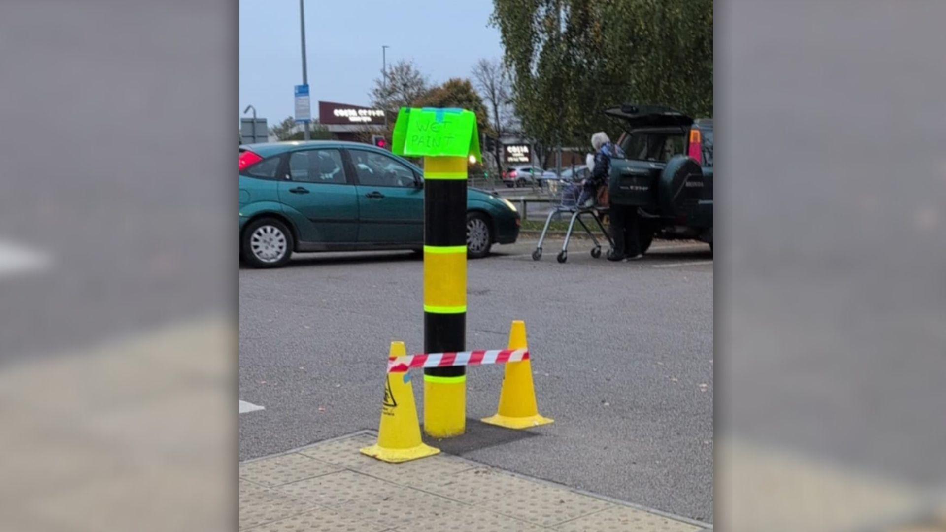 The Lidl bollard after receiving a new coat of paint, with a sign taped on warning of 'wet paint'.