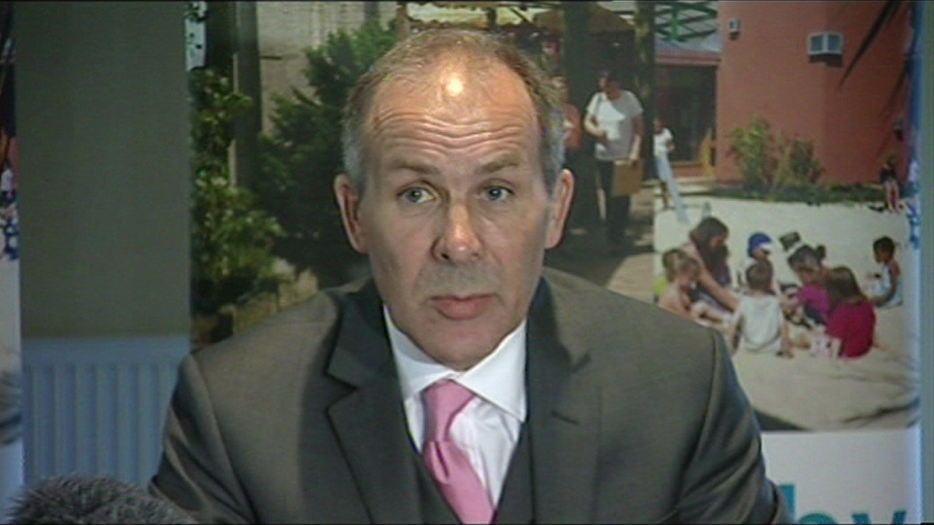 Chris Mallender in a suit with a pink tie at a press conference