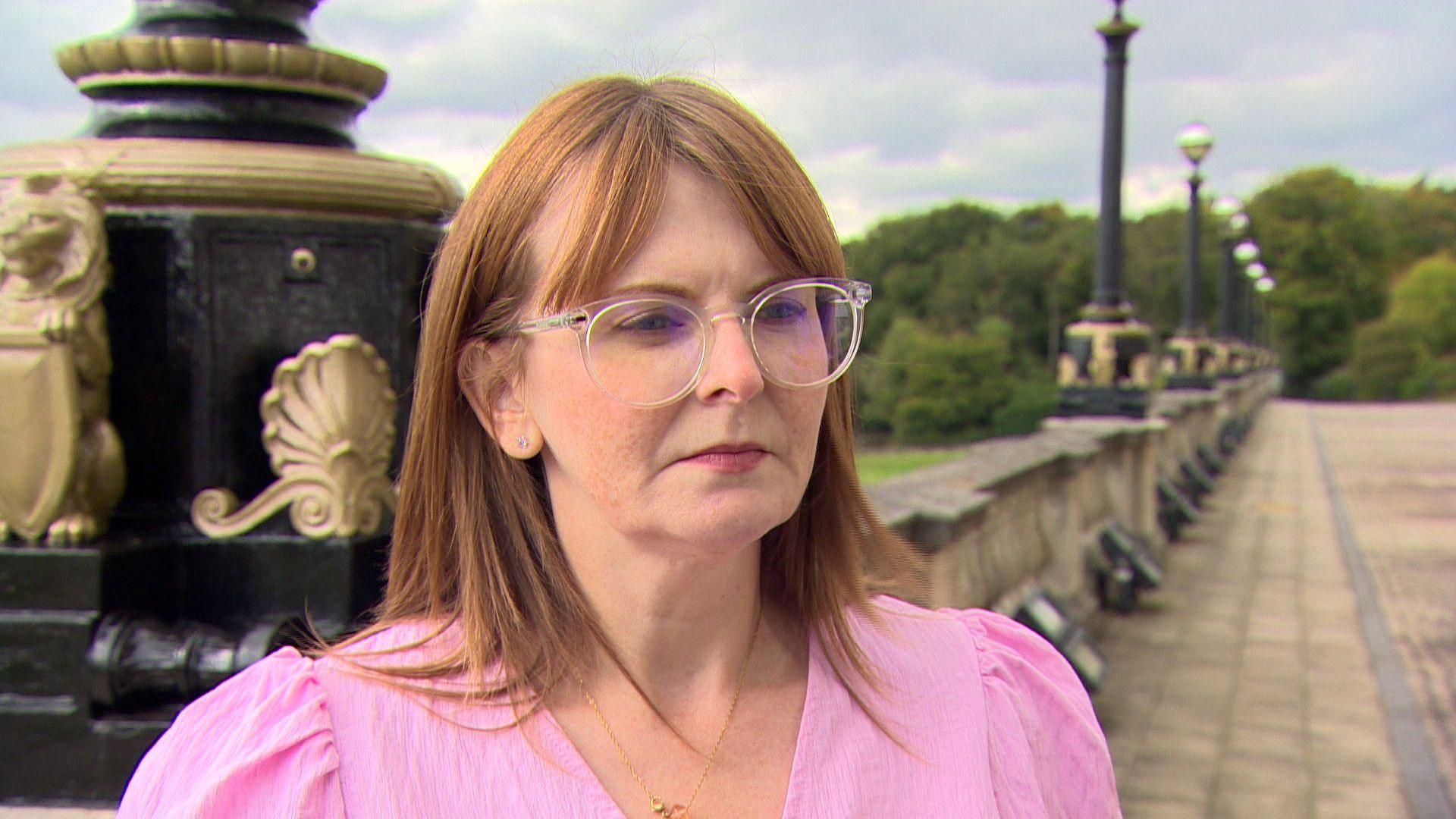 Caoimhe Archibald, a woman with red hair, glasses and a pink top is speaking at outside stormont.