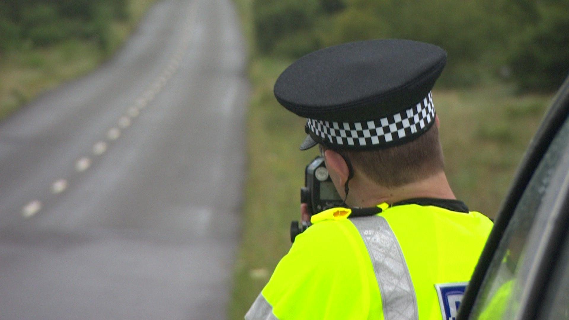 A police officer next to a single carriageway rural road with a speed gun.