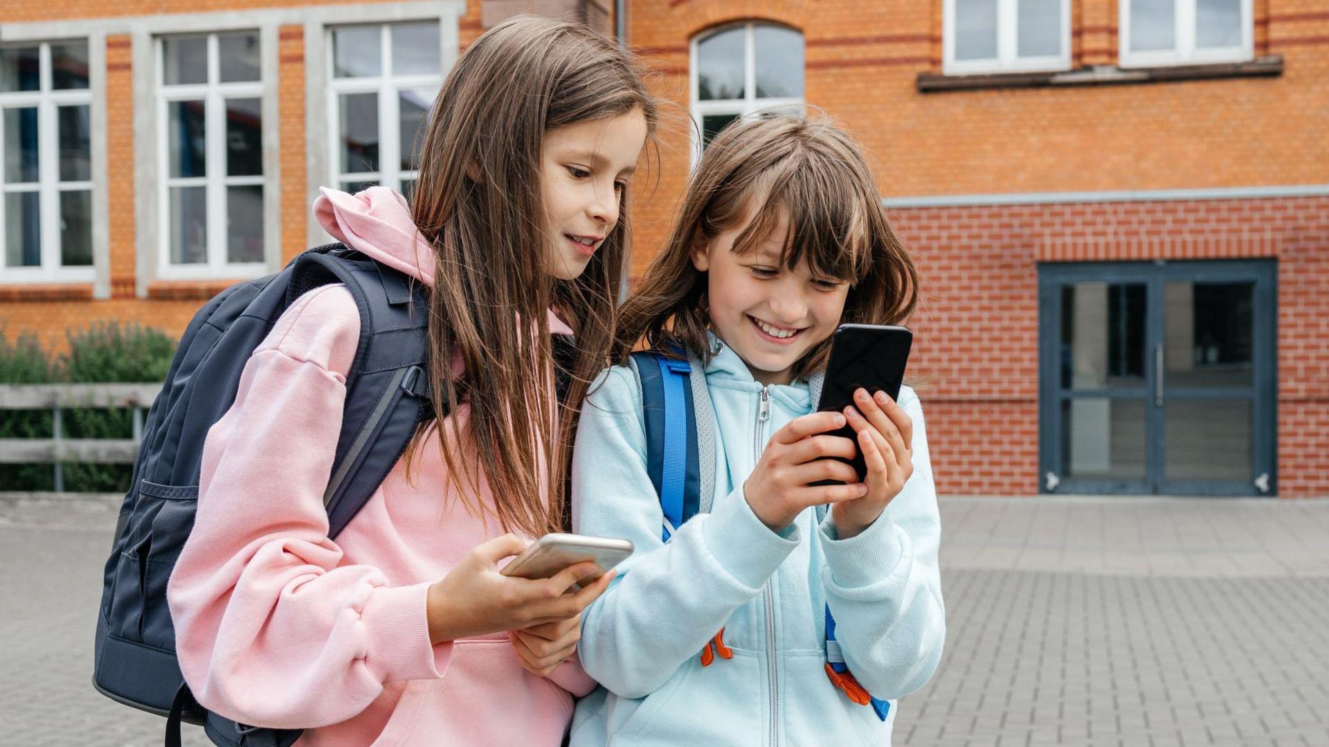 two girls holding a mobile phone and smiling at it