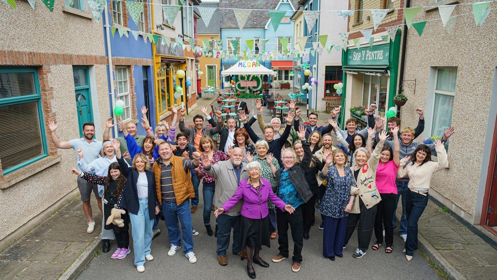 Actorion Pobol y Cwm, yn codi dwylo'n llawen ar sgwar Cwmderi i ddathlu hanner canrif o'r opera sebon.