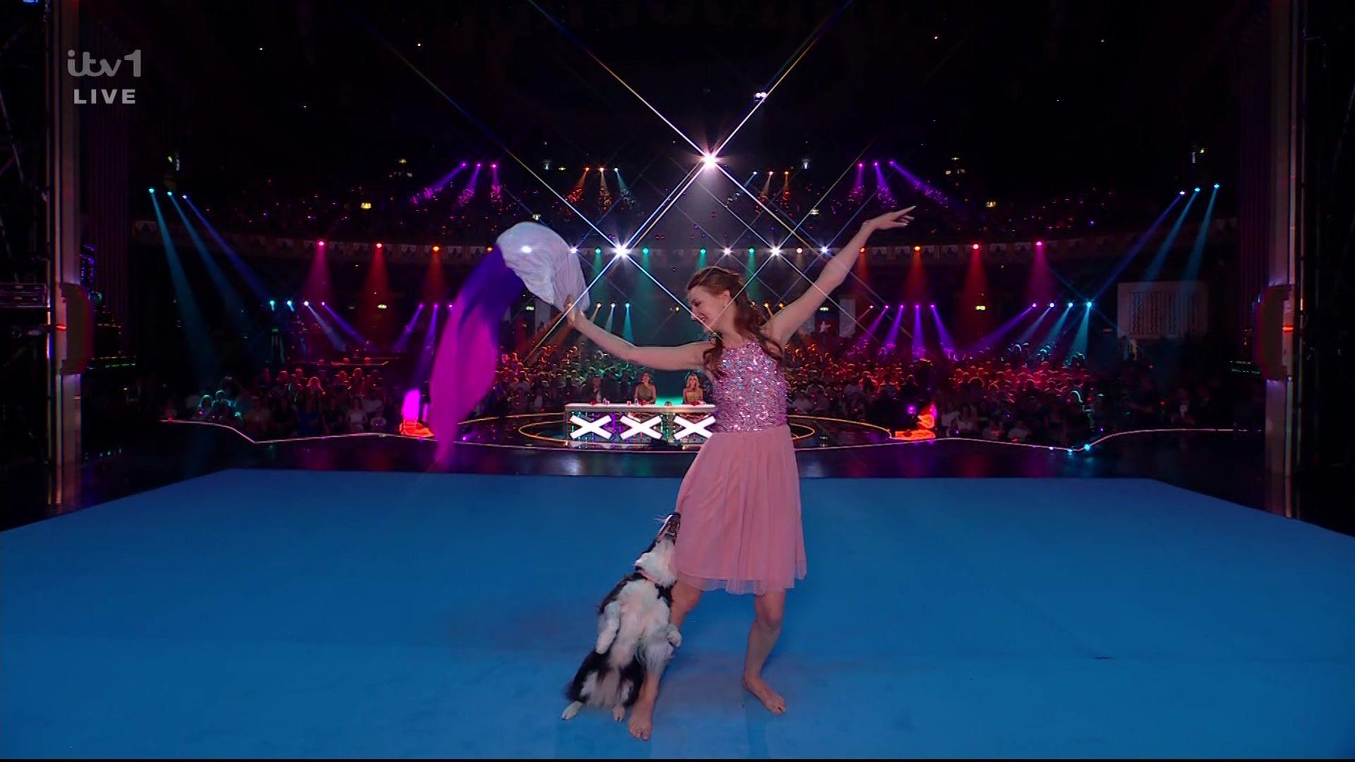 A woman and dog dance together on stage with the crowd in the background