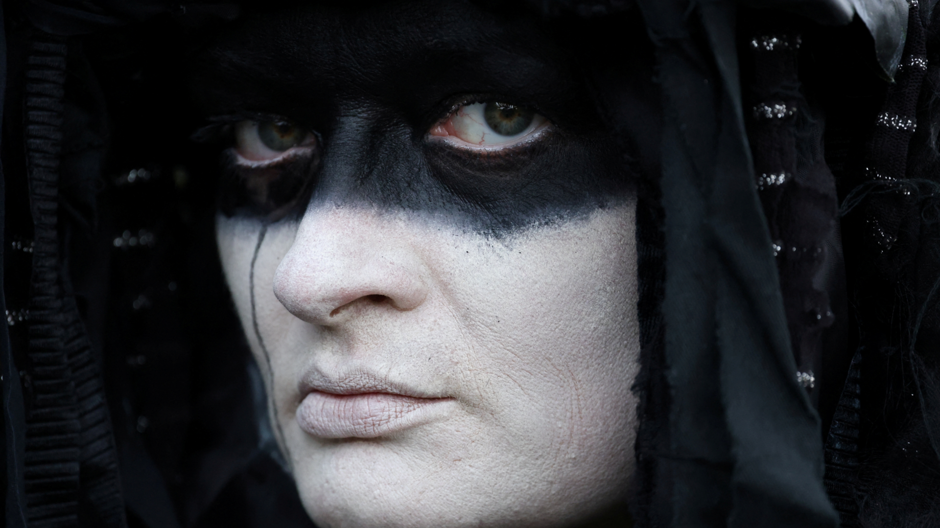 An activist of "Extinction Rebellion" (XR) dressed as an oil slick, attends a protest, in Windsor, Britain, August 30, 2024. The activist has a painted white face with a black around the eyes and wears a black hood.