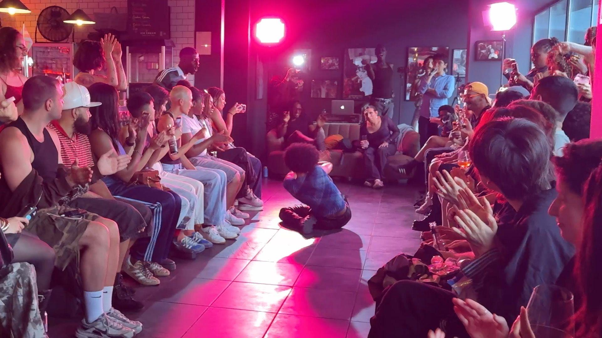 A performer vogues on the runway as observers line both sides of the floor, applauding and watching at the event.