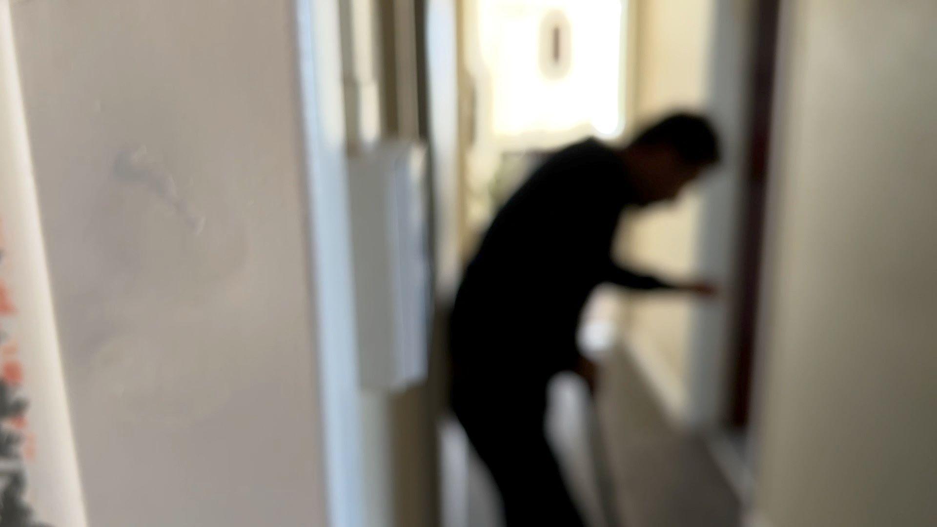 Ali in the hallway of the flat. He is seen in silhouette and is slightly bent forwards. 