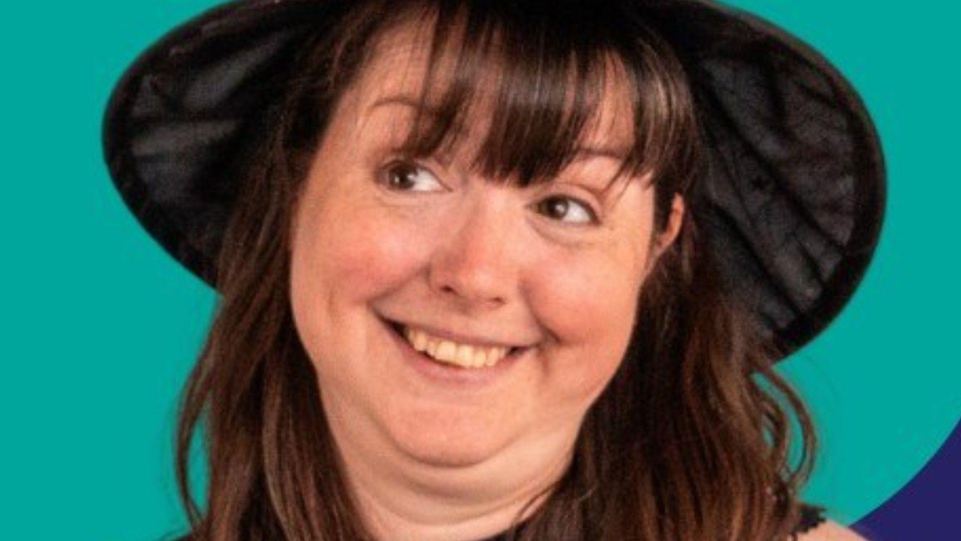 A close-up headshot of a woman with long brown hair and brown eyes wearing a black hat.