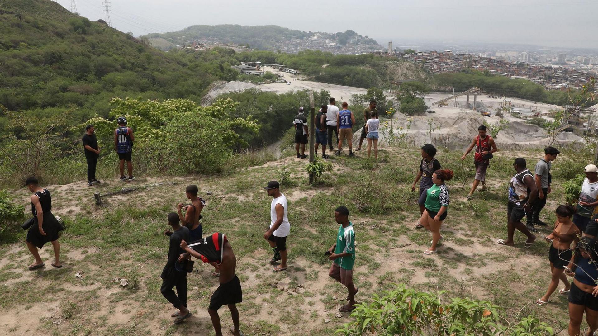 Around two dozen residents of Penha search a hillside for people who went missing after a police raid. Some of them are looking down what looks like a ravine, while others are walking.