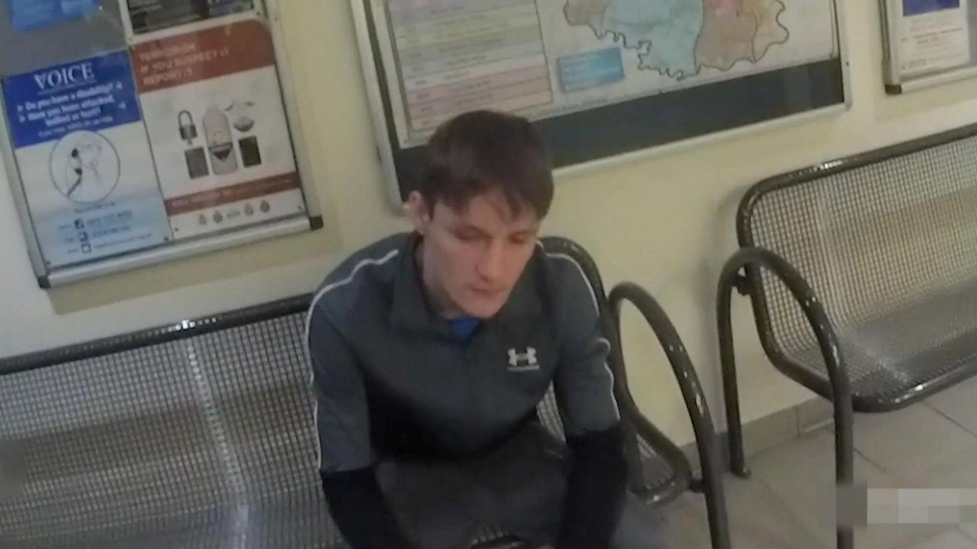 Hartle sitting on a chair in a police station wearing a tracksuit top